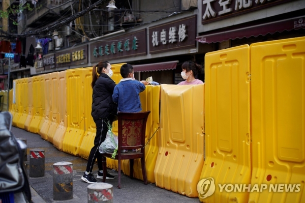 1일 우한에서 마스크를 쓴 한 여성이 건물 봉쇄 장벽 너머로 채소를 사고 있다. [출처=연합뉴스]