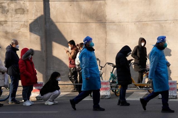 지난해 12월 9일 중국 베이징의 한 병원 열병진료소 앞에 환자들이 줄을 선 가운데 방역복을 입은 의료진이 지나가고 있다. [사진 = 연합뉴스]