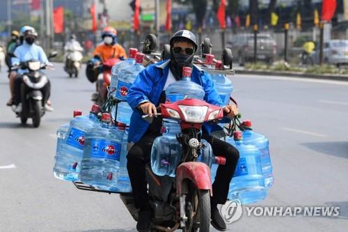 폭염 속에서 수요가 급증한 물통을 주렁주렁 달고 배달하는 베트남 오토바이 택배근로자 [사진 = 연합뉴스]
